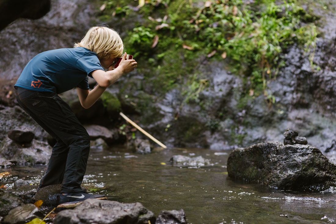 boy taking photos in a stream in hawaii