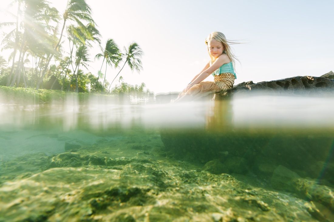 girl sitting on a rock in the water at paradise cove lagoon in koolina