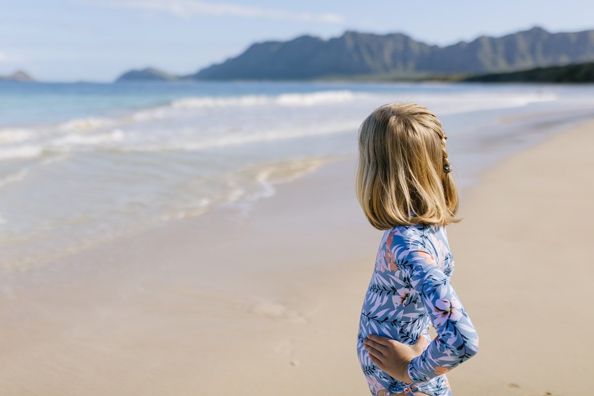 girl looking at the water with mountains in the background at bellows beach in hawaii