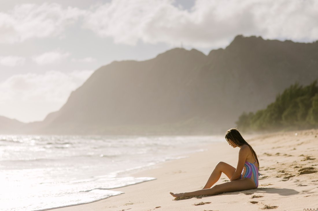 portrait of a girl sitting on the sand at sunrise at waimanalo beach hawaii