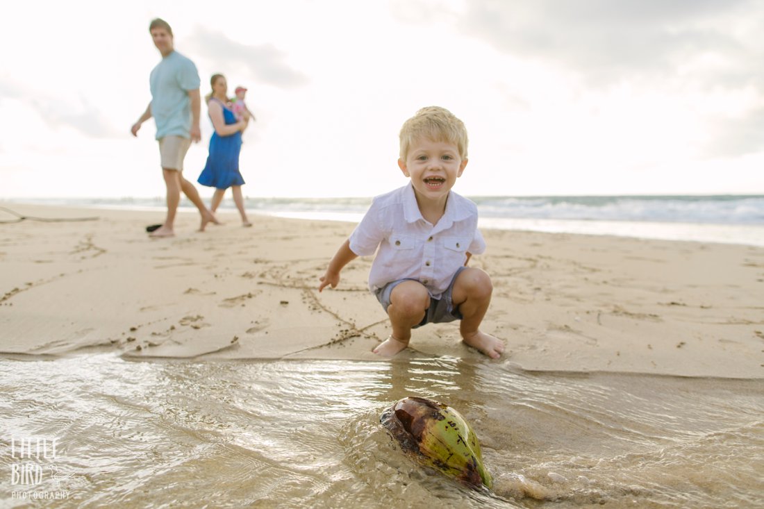 boy playing witha coconut at the beach while parents look on