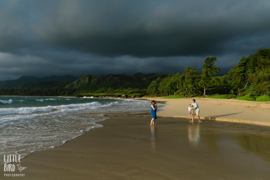family playing on the beach in hawaii against a dramatic stormy sky