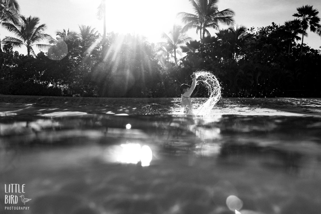 boy splashing water at ko olina lagoon in black and white photo by Little Bird Photography