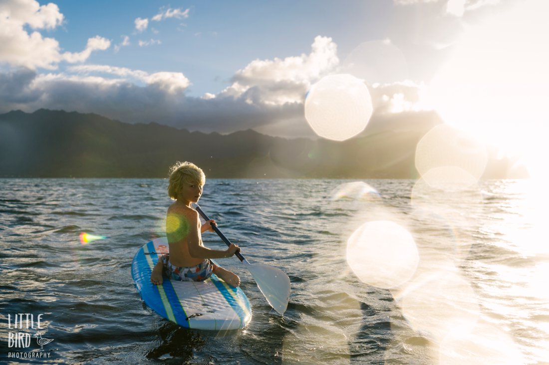 boy on a sup in kaneohe bay at sunset with water bokeh