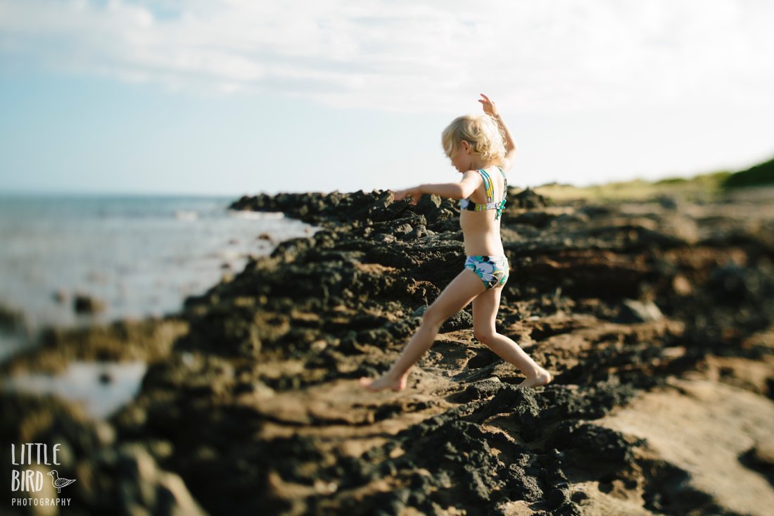 girl jumping over rocks along the rocky shore of Hawaii