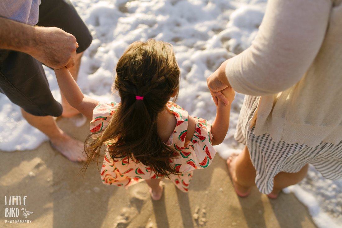 toddler holding hands with parents as waves wash over their feet