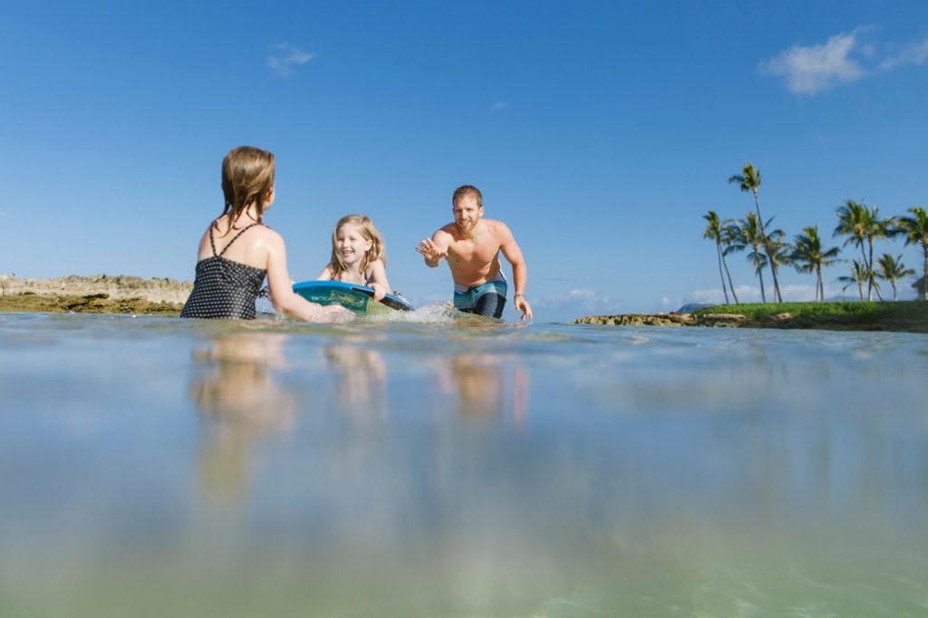 family plays in the water at paradise cove in koolina