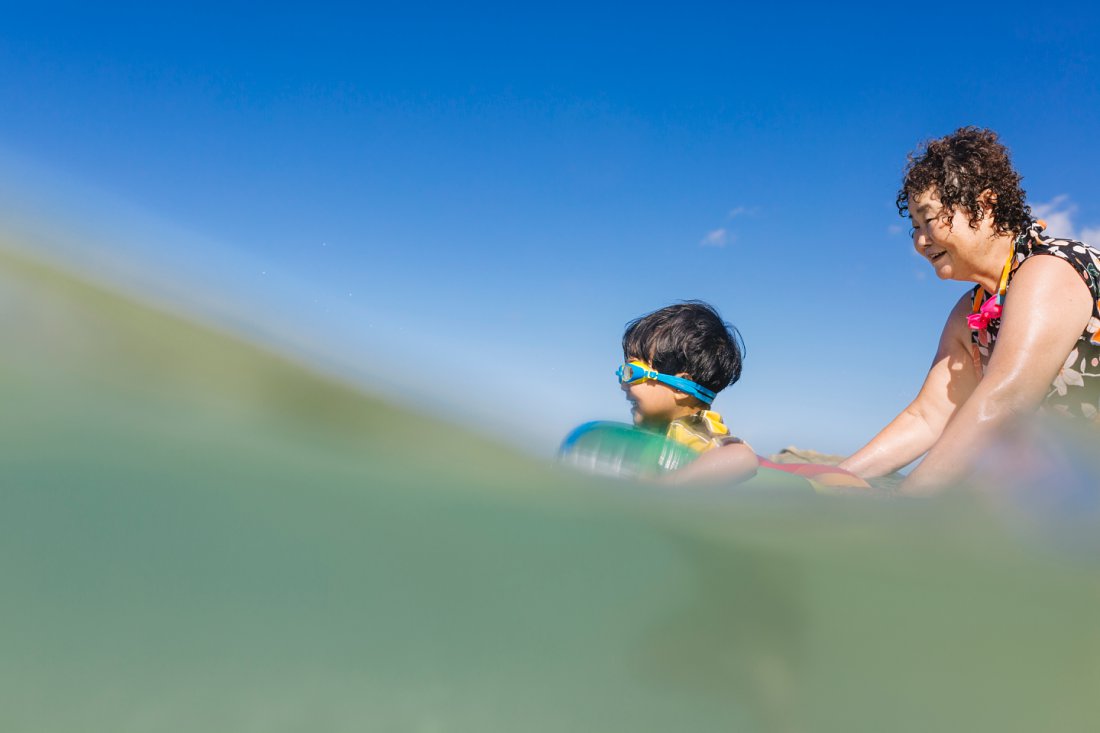 grandma pushing grandson in blue waters of oahu hawaii