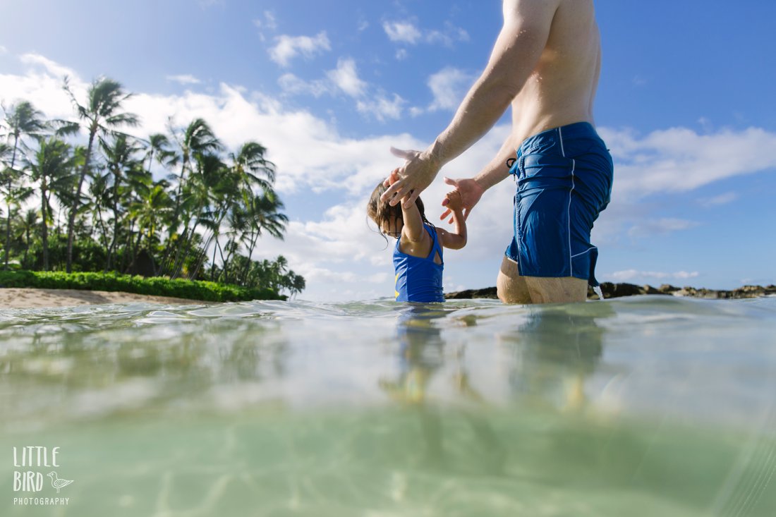 dad and daughter play in clear blue water in oahu