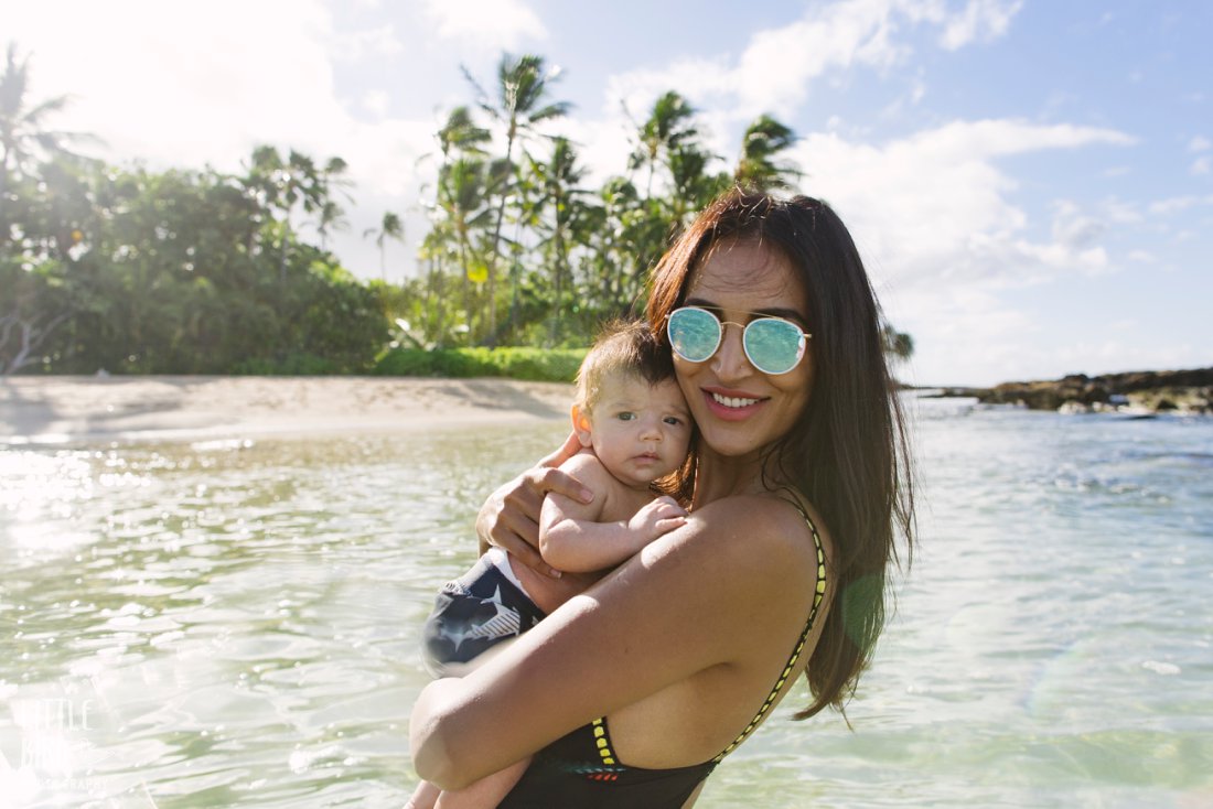 mom happily snuggling newborn baby in the water at paradise cove beach in oahu