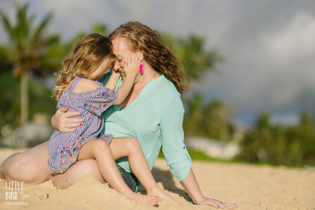 mom and daughter snuggle during family beach photoshoot in hawaii