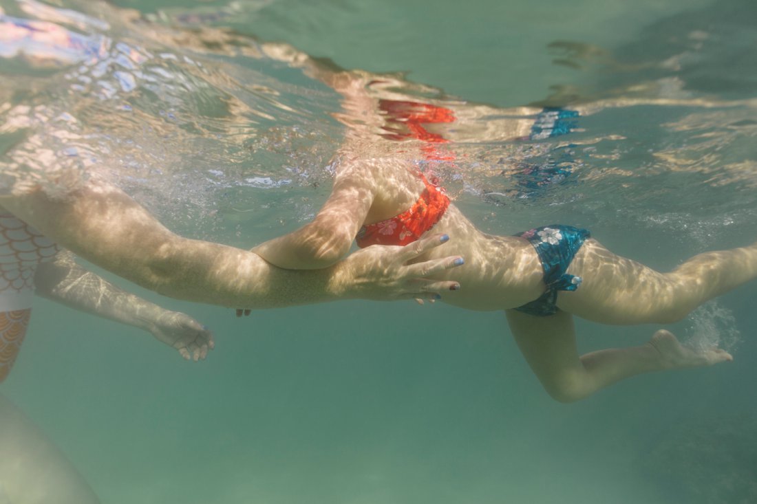girl swimming to mom in clear blue waters of hawaii
