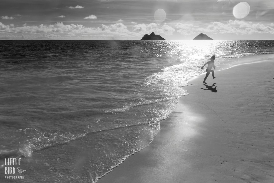 girl running on the beach with mokuluas in the background