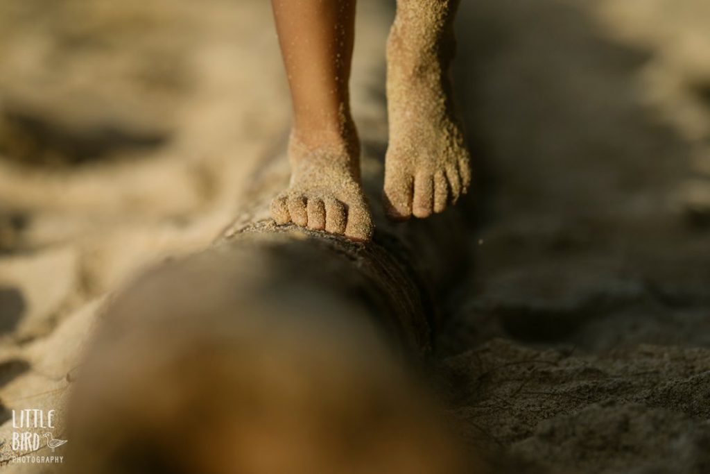 sandy feet walking on a log at a beach in hawaii