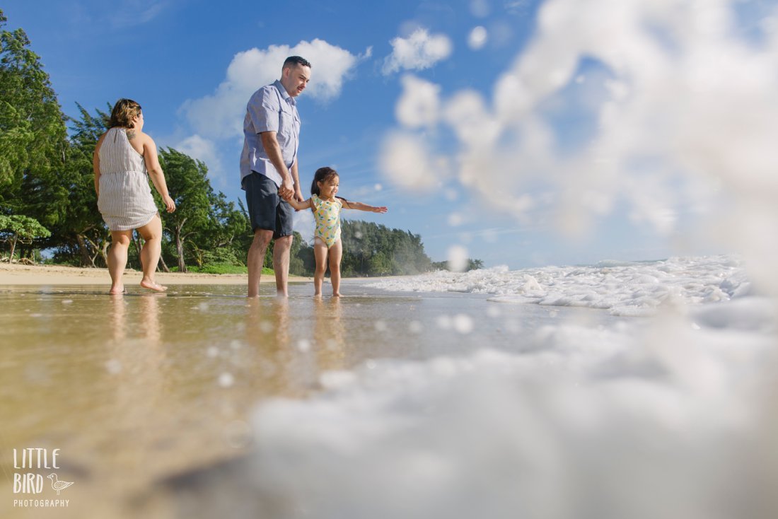 family plays on the beach in hawaii as waves pound the shore