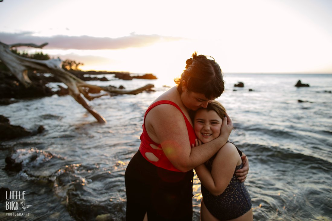 mom and daughter cuddle at sunset at waialea beach on the kohala coast of hawaii