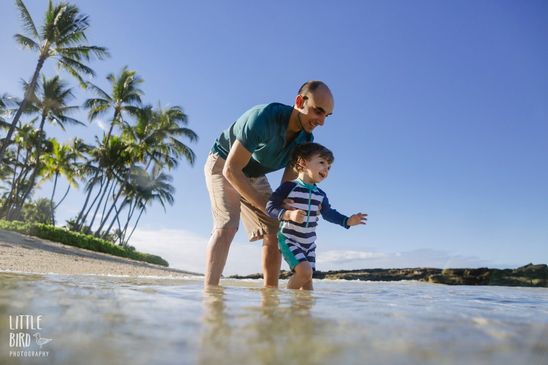 dad and son splashing in the shallows at paradise cove koolina