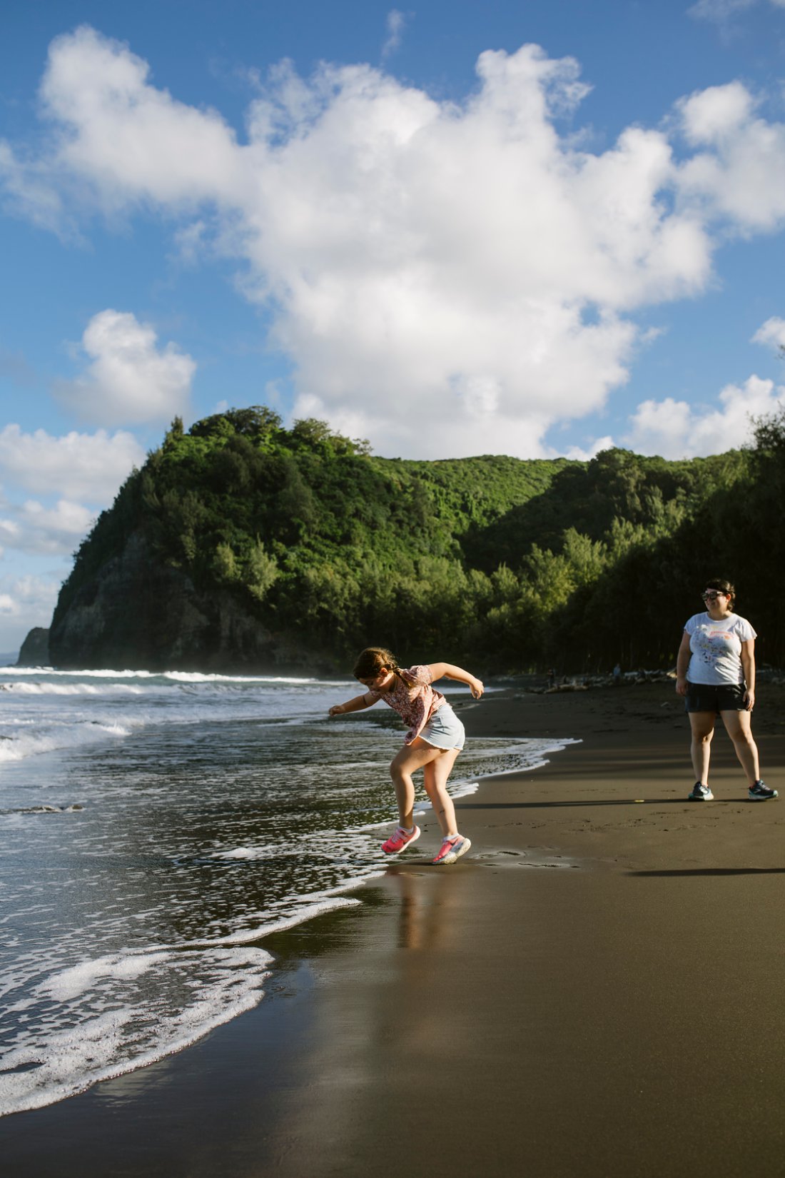 mom and daughter playing on a black sand beach in hawaii