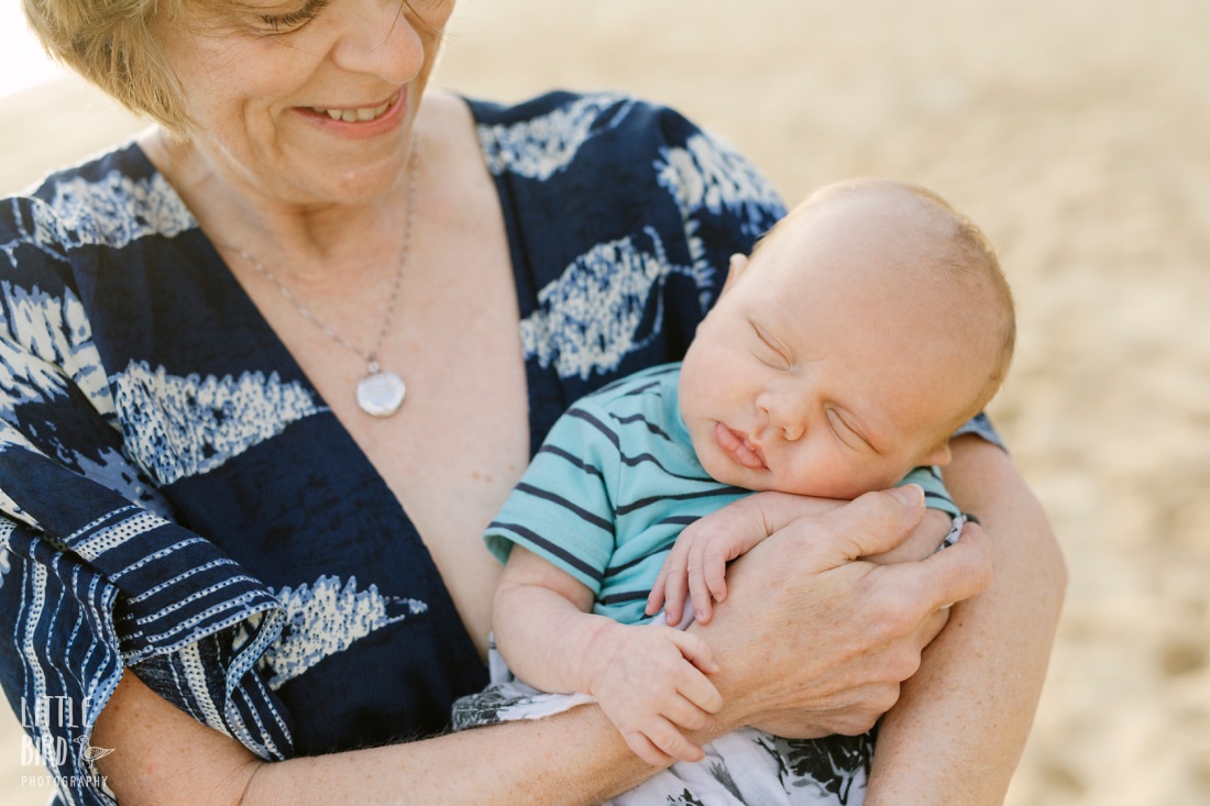 grandma proudly holds new baby at the beach
