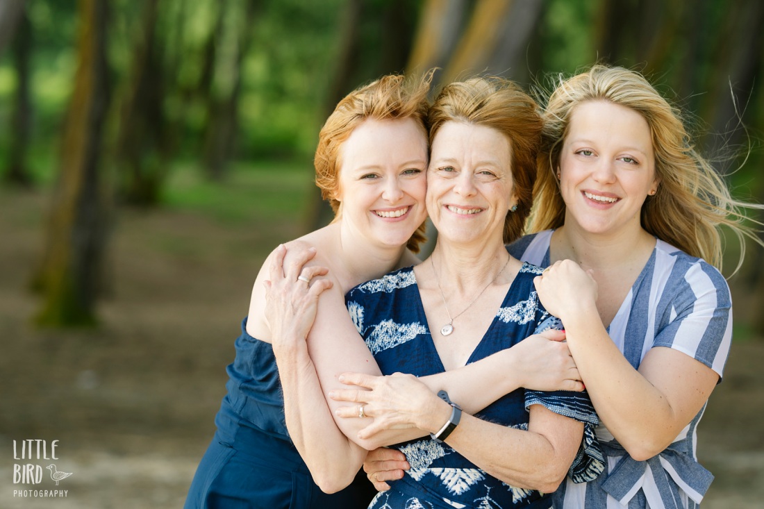 mom and her adult daughters hug at the beach during a family photoshoot