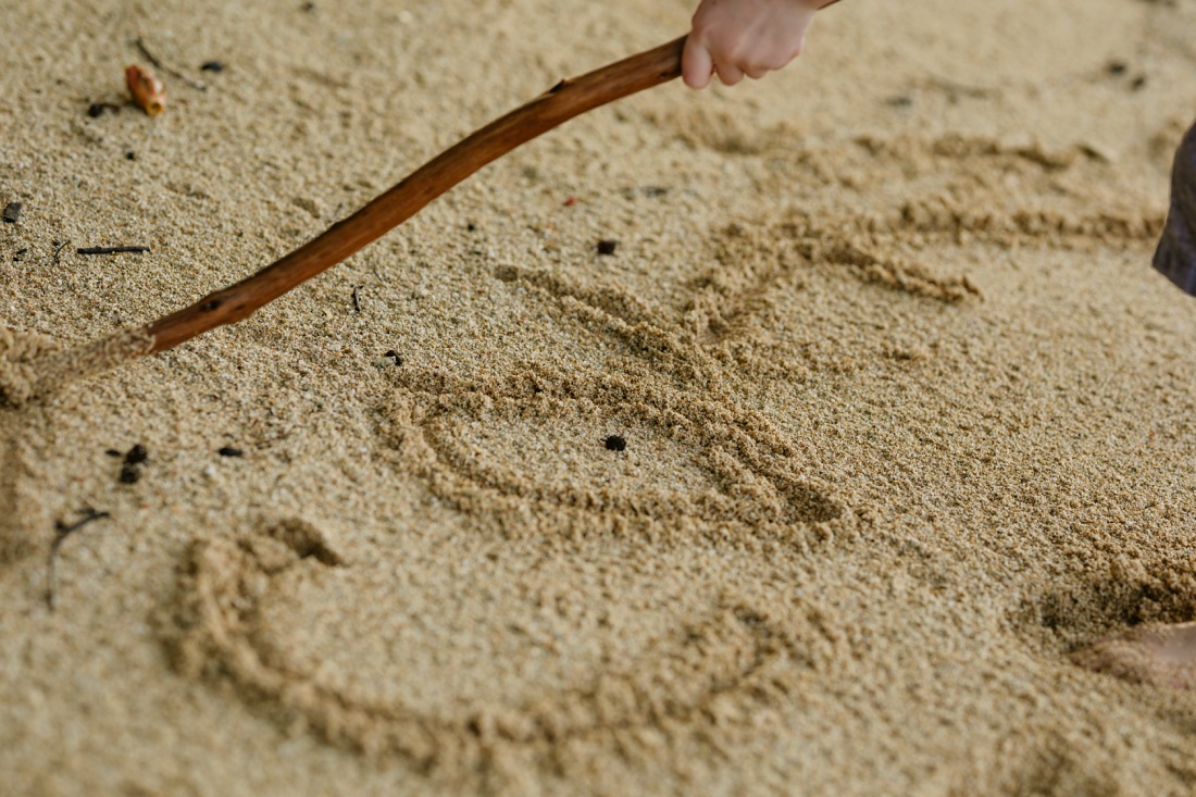 boy writing his name in the sand with a stick