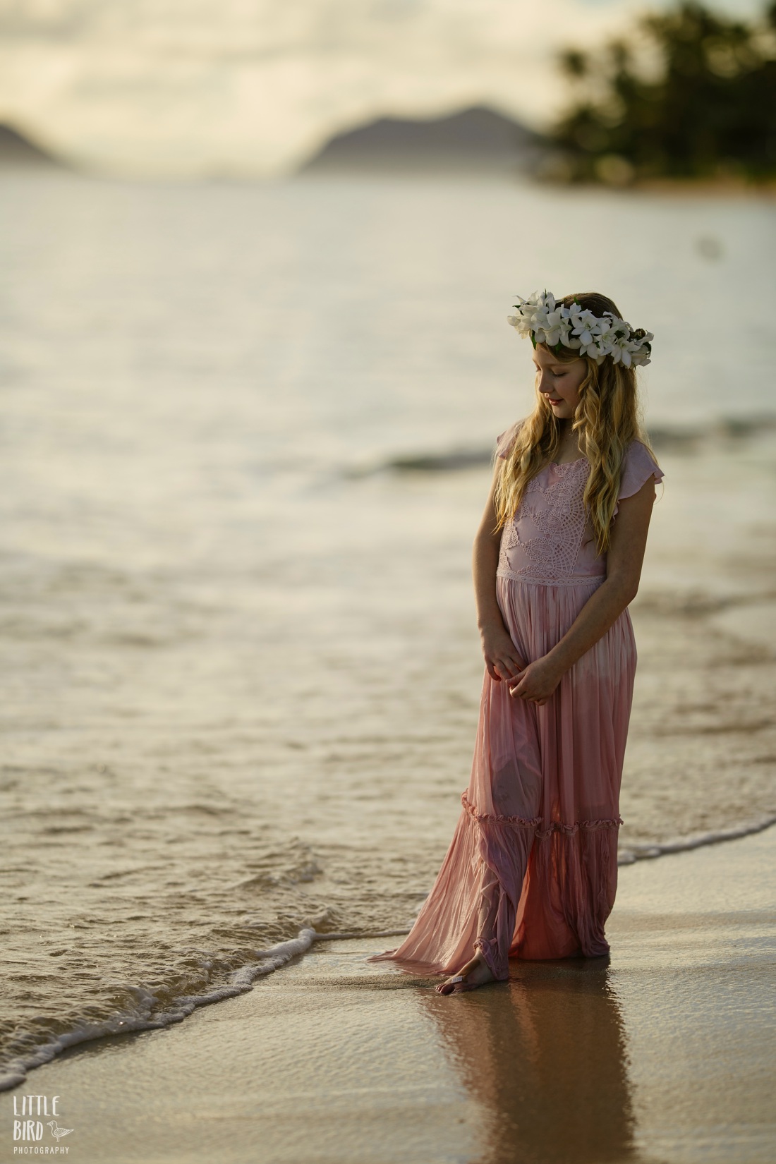 girl wearing a haku lei stands by the water at sunrise in lanikai during a family photoshoot