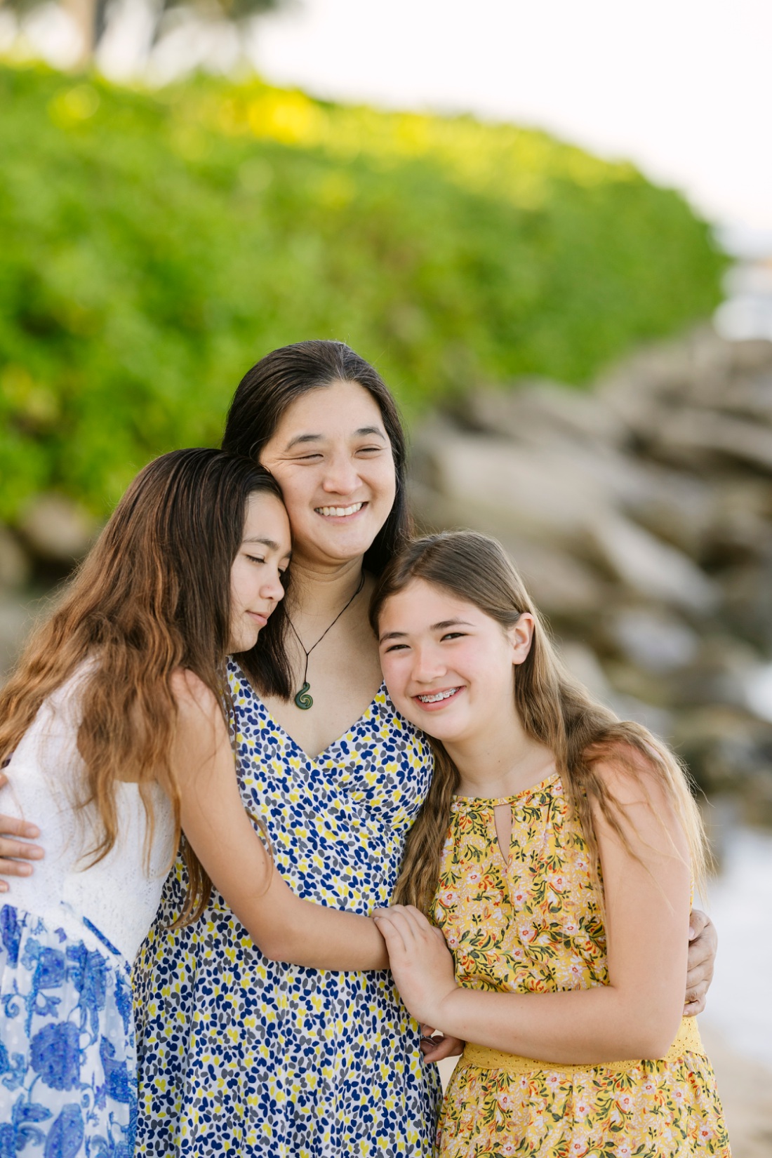 mom and daughters share a hug at the beach in hawaii during a family photoshoot