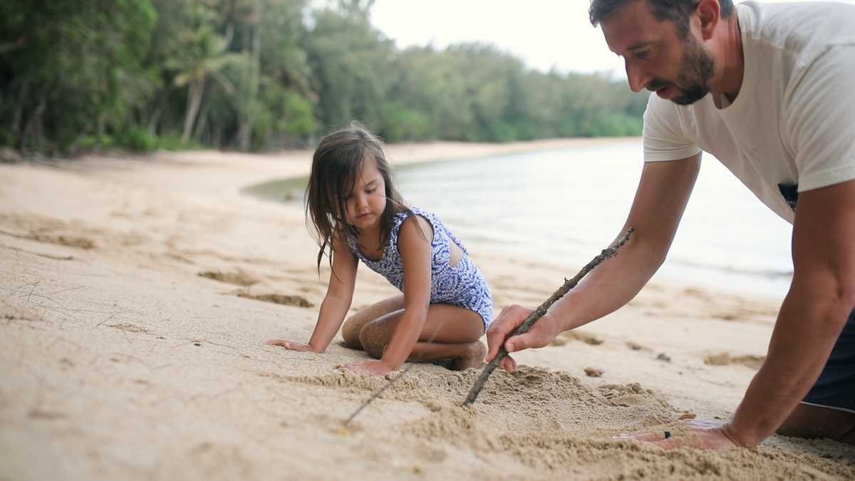 dad and daughter writing in the sand at kawela bay oahu