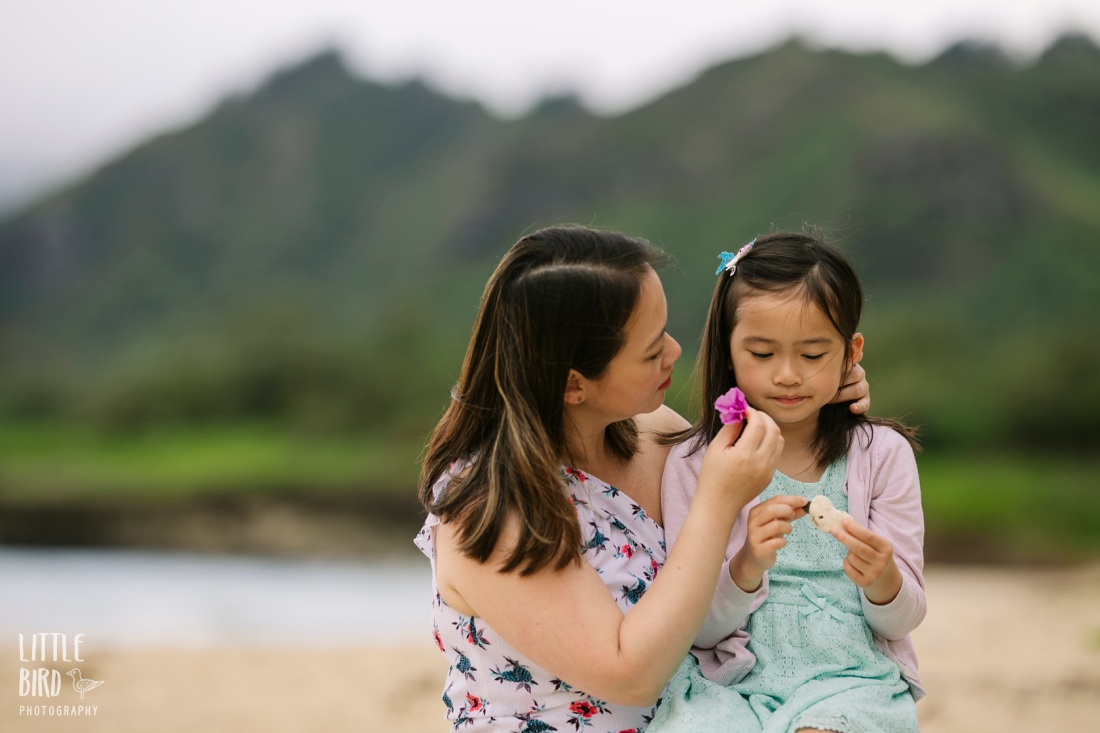 mom puts flower behind daughter's hair during a family photo session in hawaii
