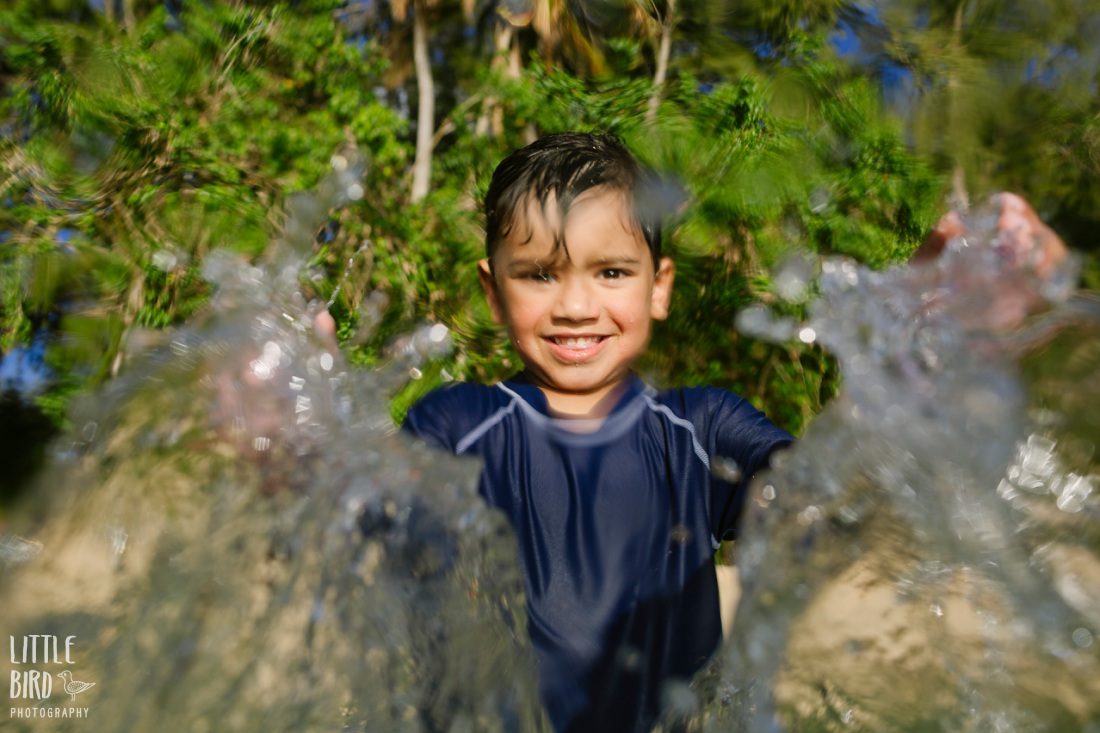 boy splashing water at the camera during a family photo session in hawaii