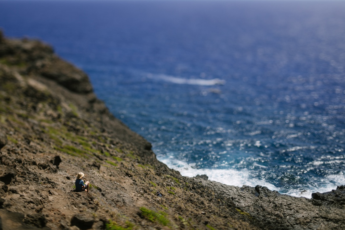 boy sitting on the rocks along a cliff hike with ocean views in hawaii