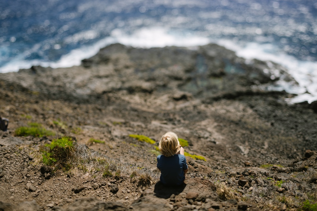 boy sitting on the edge of a steep hike to the makapuu tide pools trail on oahu