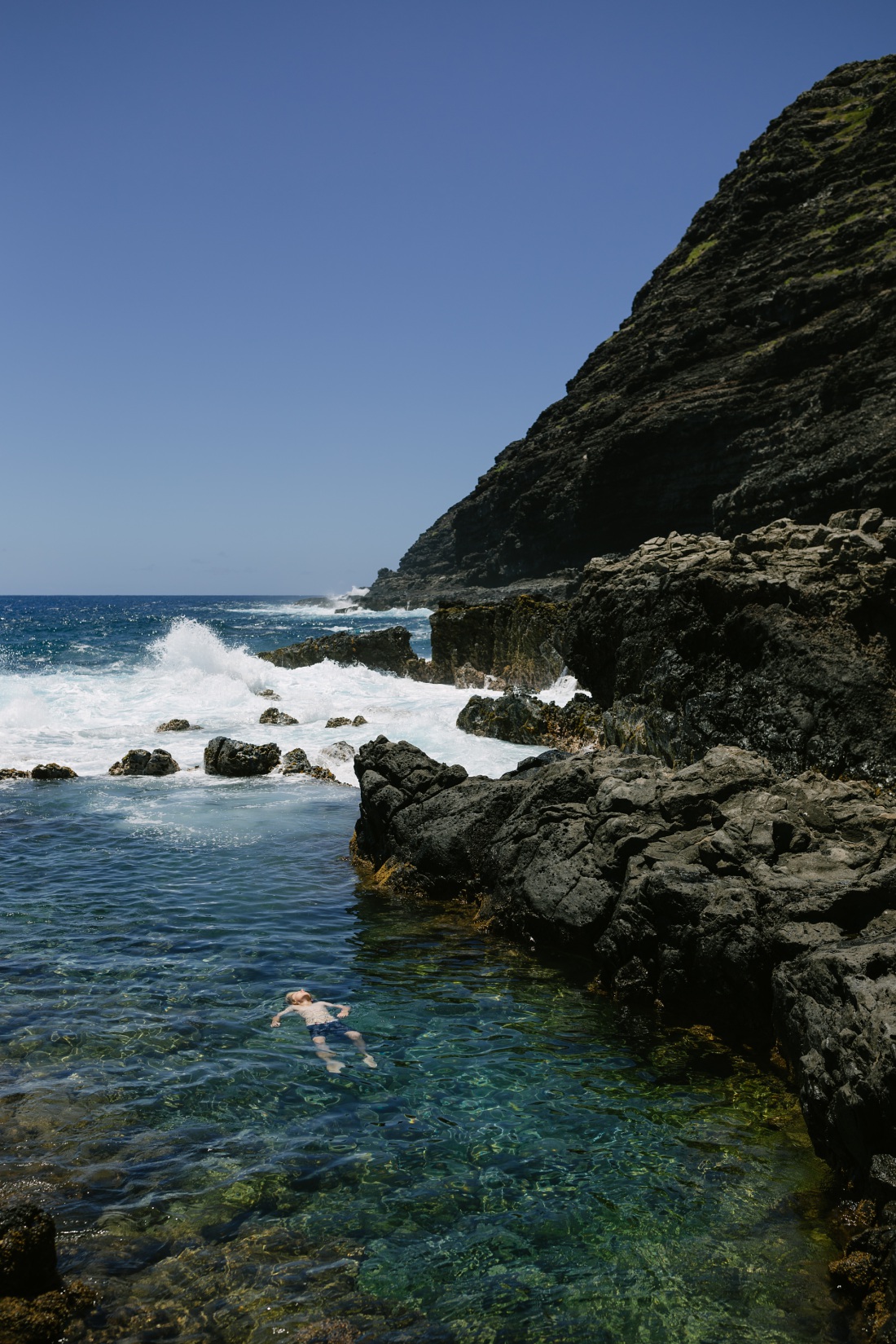 boy floating in the tide pools at the makapuu trail with cliffs in the background