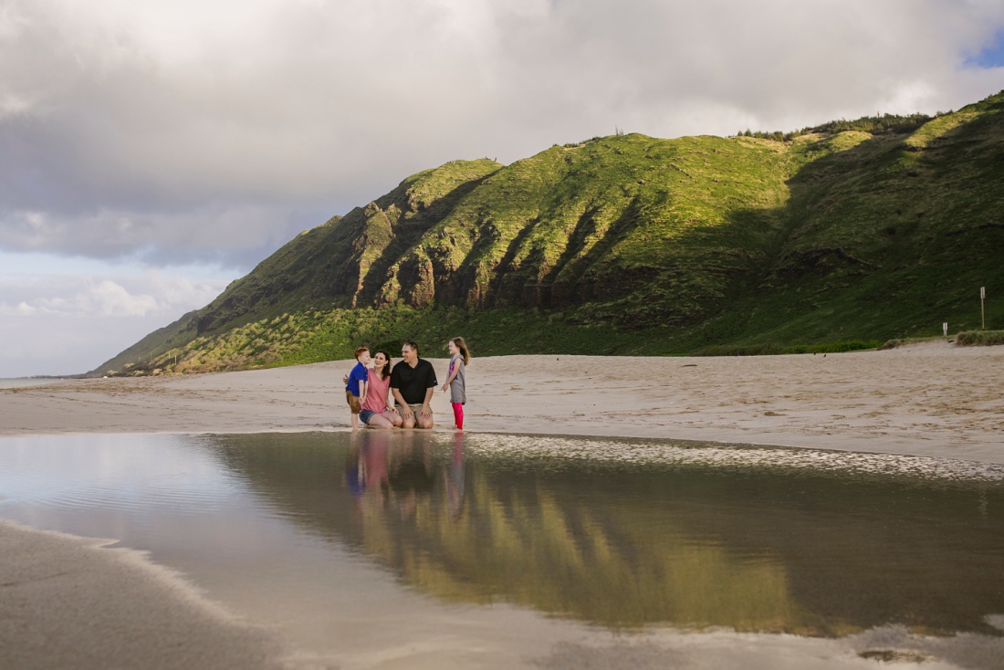 family sitting on the beach with reflections of mountains at yokohama bay oahu