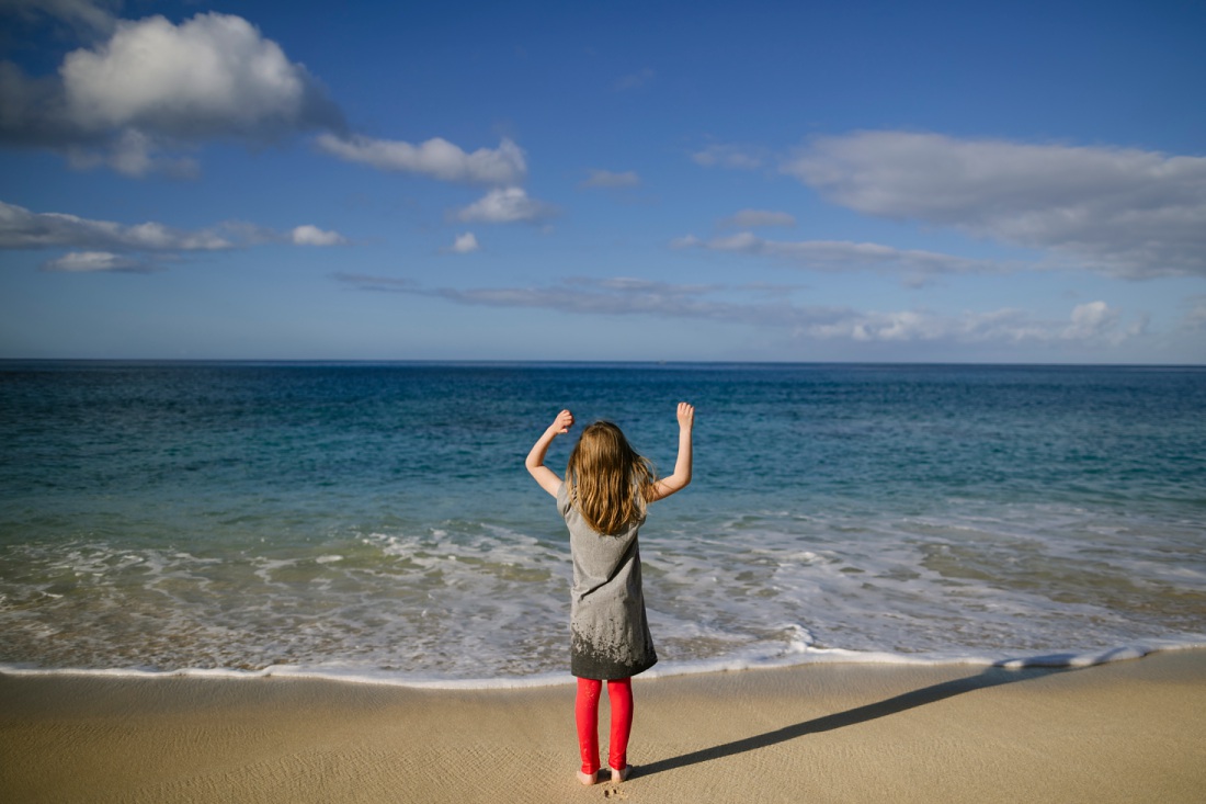 girl waving to the waves with blue ocean and sky