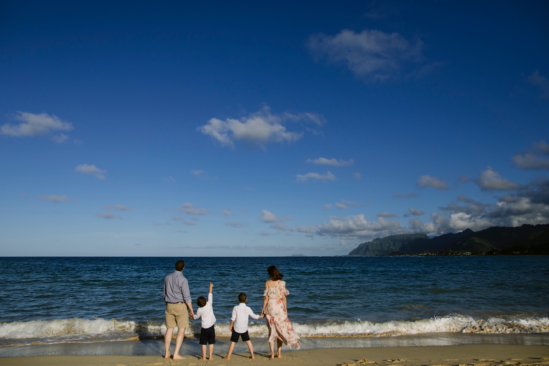 family playing at the edge of the ocean in oahu with mountain view in the distance