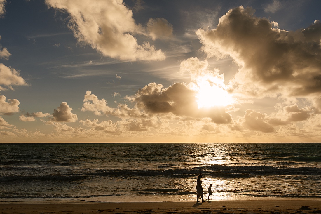 silhouettes of mom and son walking on Waimanalo Beach at sunrise