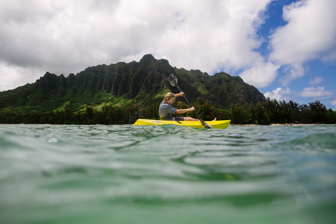 boy kayaking in kaneohe bay with kualoa mountains behind