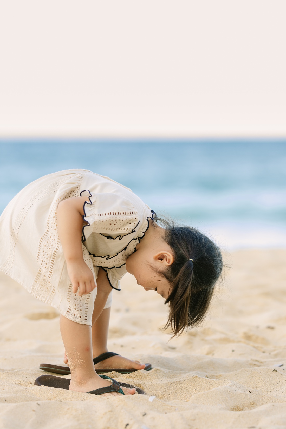 little girl with big slippers on the beach