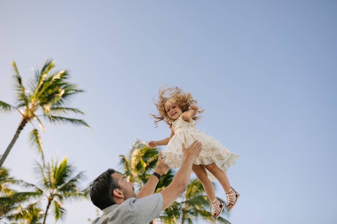 dad tossing daughter in the air with palm trees behind