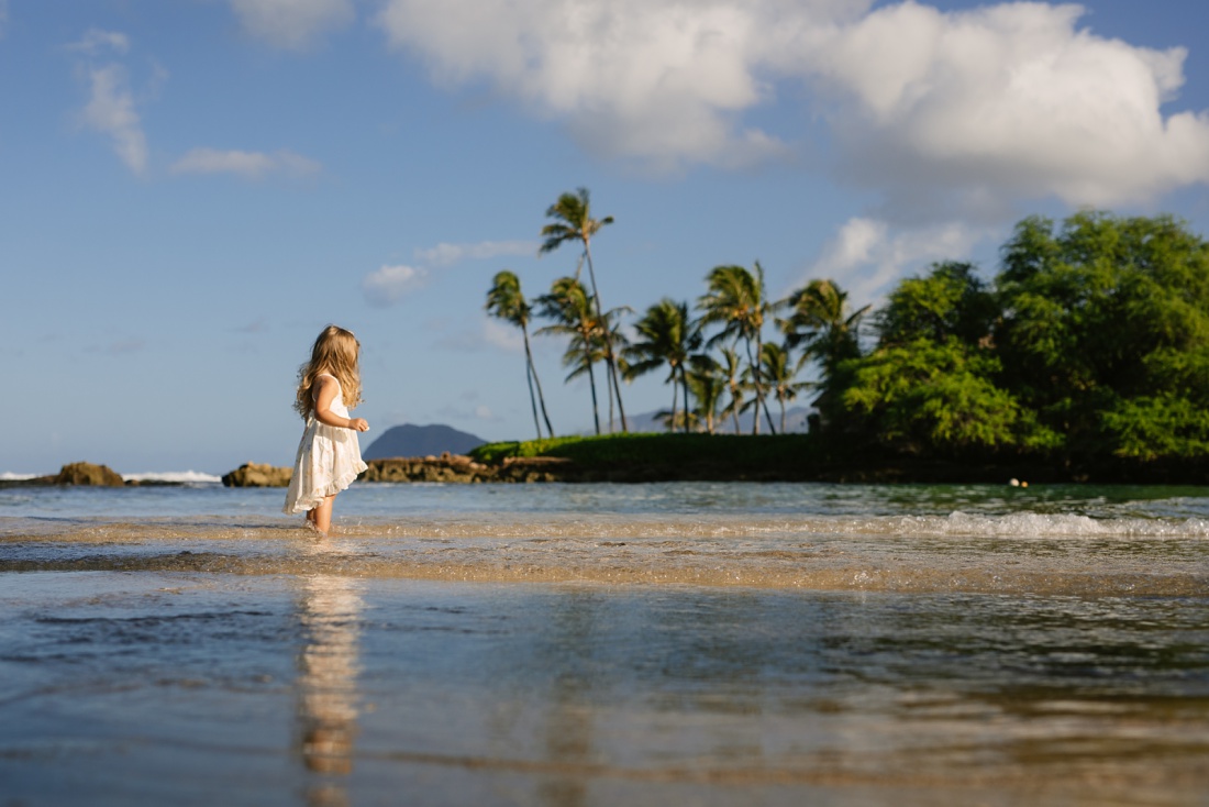 girl standing in shallow water at a beach in hawaii with reflection