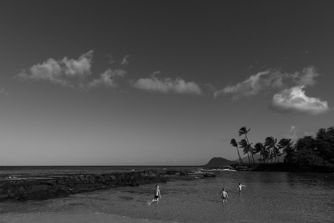 black and white landscape with boys running in the water at paradise cove in oahu, hawaii