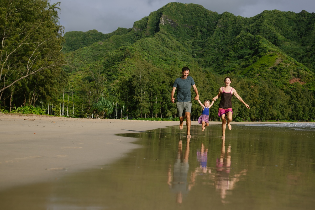 family running on Kahana Beach with mountains behind and reflections
