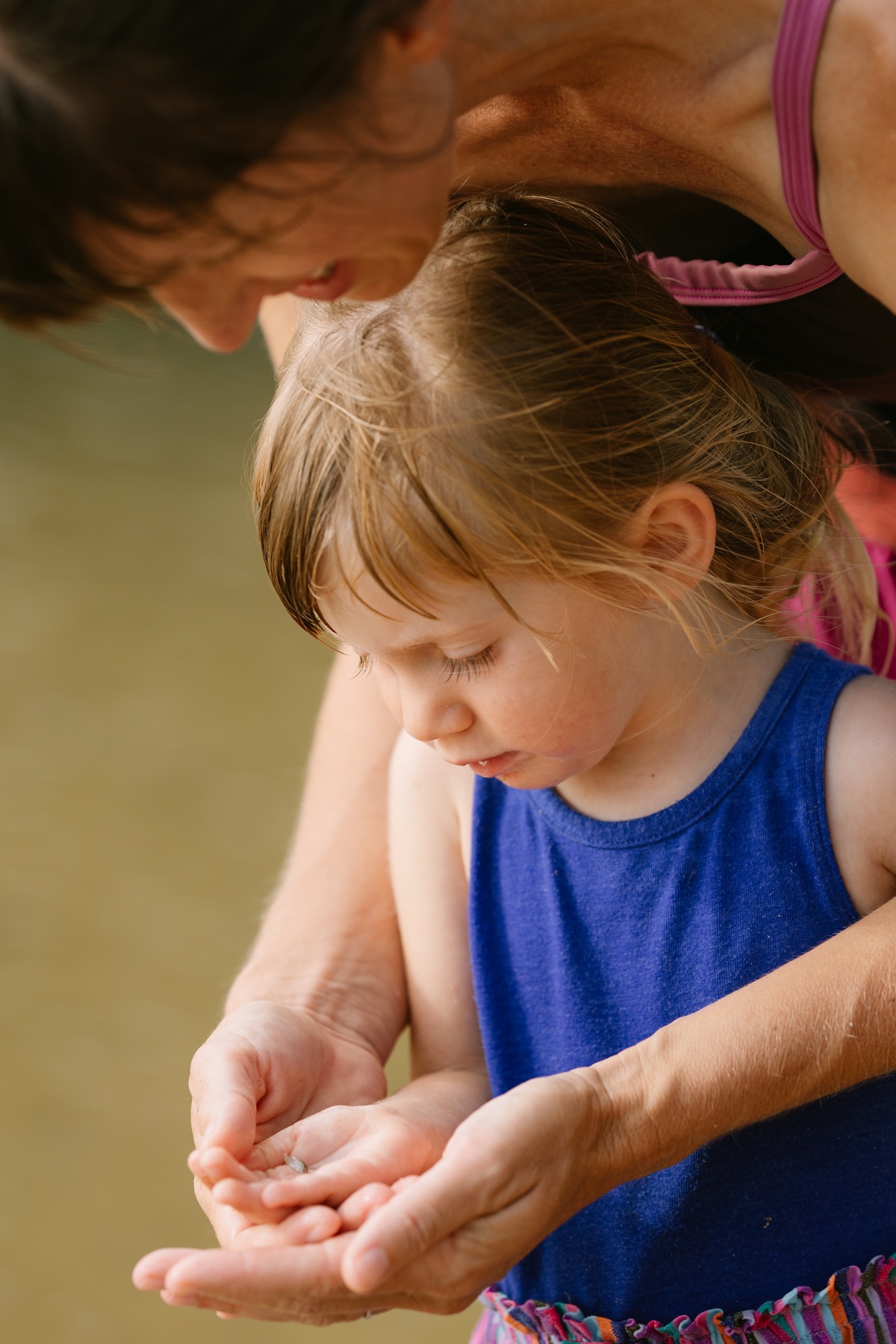 mom showing toddler daughter a tiny fish during a family adventure photography session