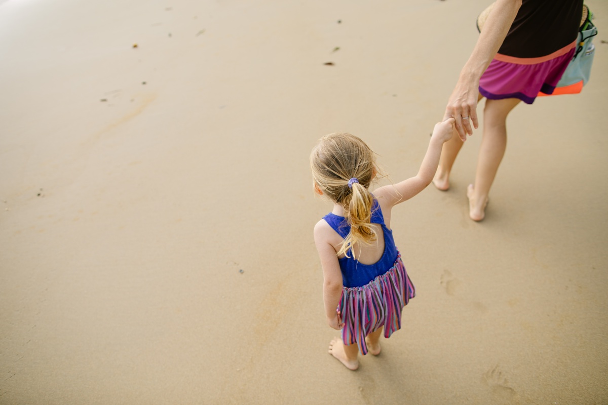 mom and daughter holding hands on the beach