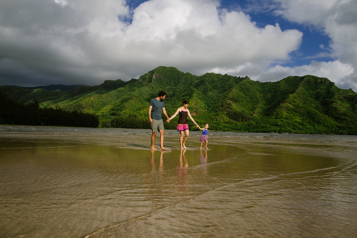 family walking in kahana bay at low tide with reflections and mountains in the background