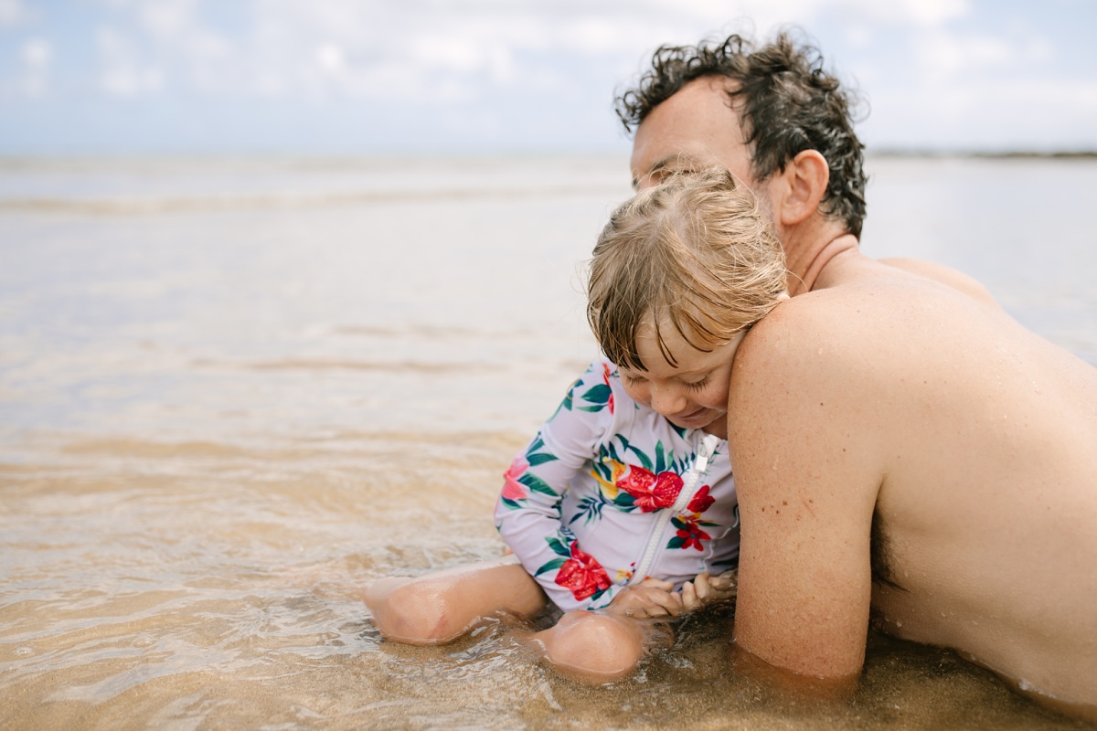 toddler girl snuggling up to dad during a beach photo session in hawaii