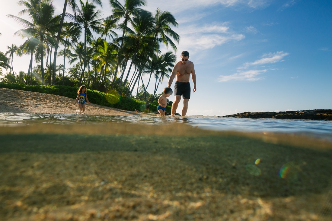 dad leading kids into the shallow blue waters in hawaii