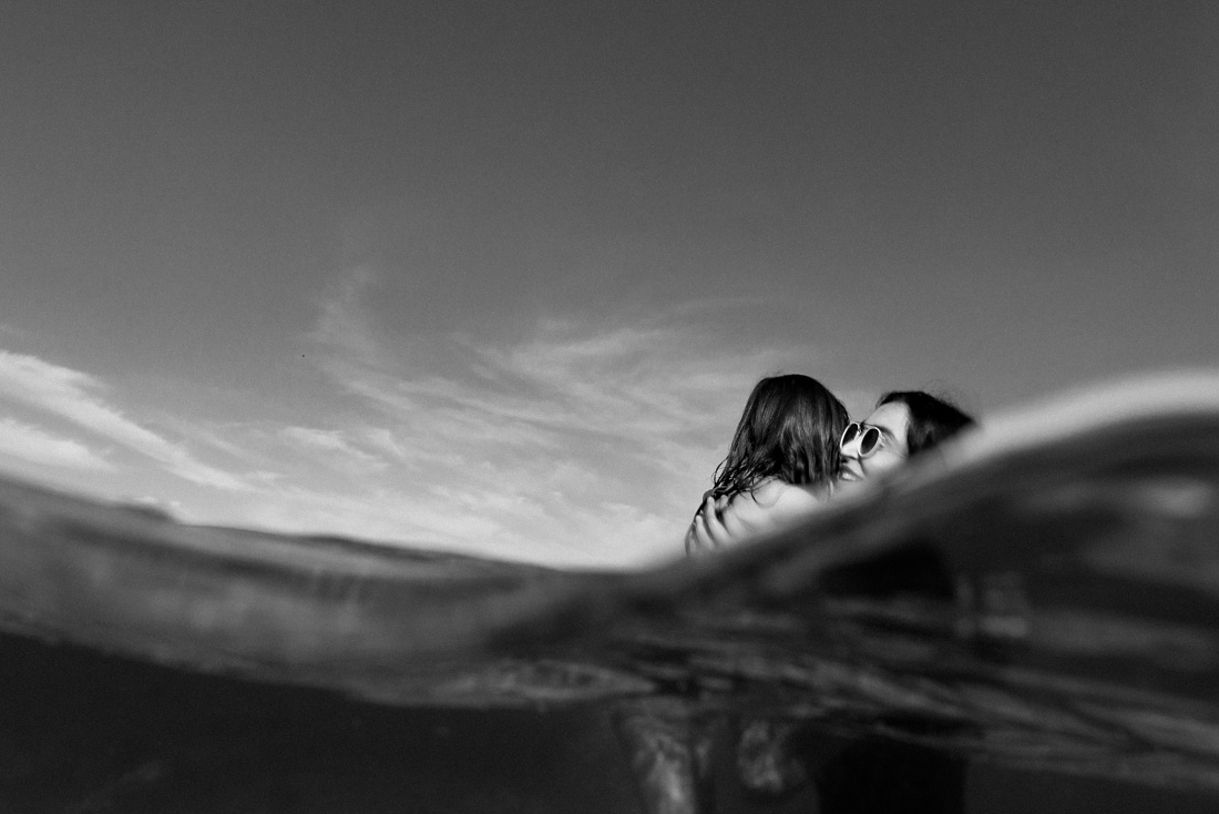 mom hugging daughter in the water in hawaii bnw portrait