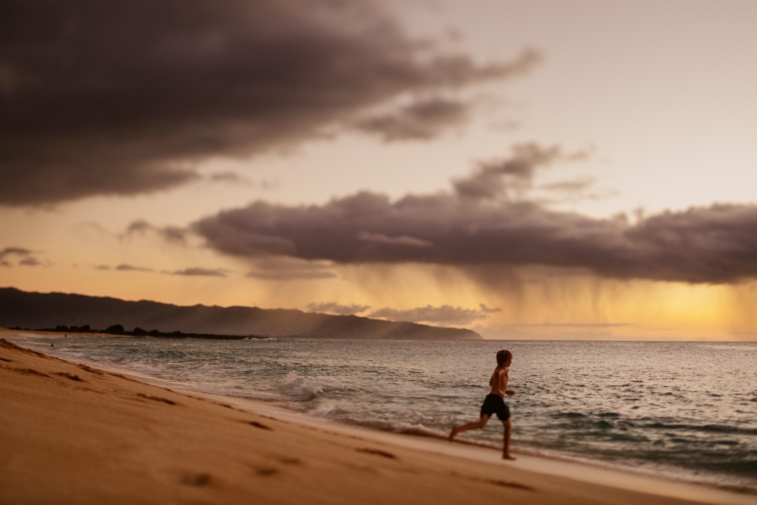 boy playing on the beach at sunset on the north shore of oahu with storm clouds offshore